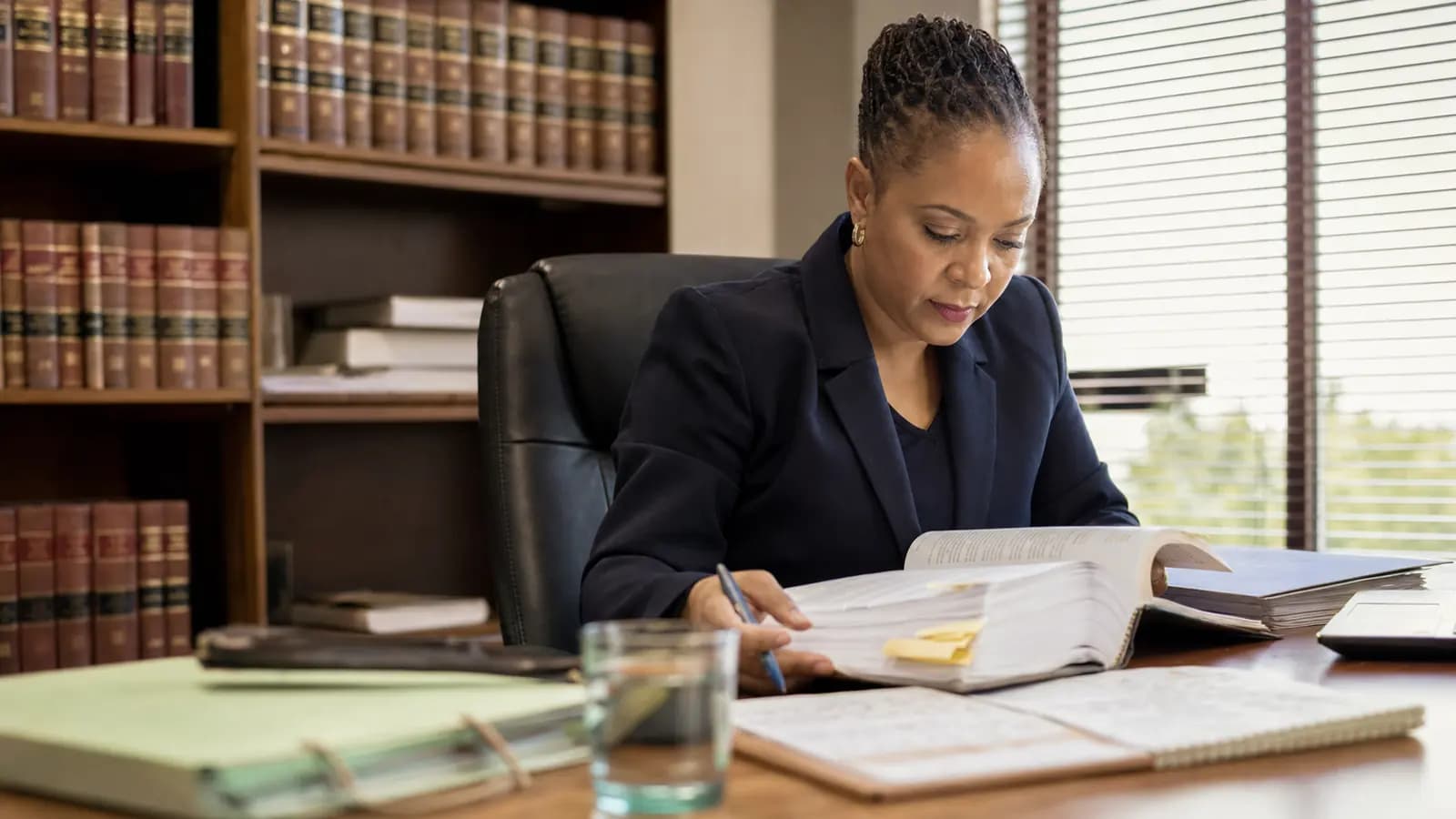 South African compliance professional reviewing legal books and a statute binder in her office
